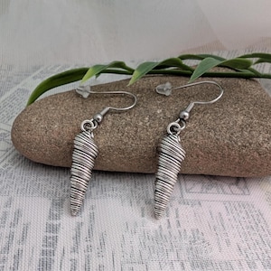 Peut inclure: Une paire de boucles d'oreilles argentées. Chaque boucle d'oreille présente un design conique enveloppé de fil métallique, suspendu à un crochet simple. Les boucles d'oreilles sont présentées sur une petite pierre texturée, avec des feuilles vertes en arrière-plan.
