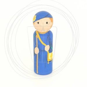May include: A hand-painted wooden peg doll dressed in a blue robe with a yellow sash and a gold pouch. The doll is wearing a blue hat with a gold star.