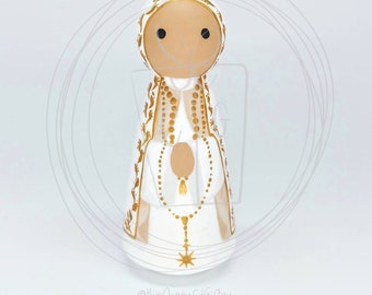 May include: A white wooden doll with a gold painted dress and a gold rosary. The doll has a brown face and black eyes. The doll is wearing a white head covering with gold trim.