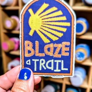 May include: A blue and orange fabric patch with a yellow scallop shell and the text "Blaze a Trail".