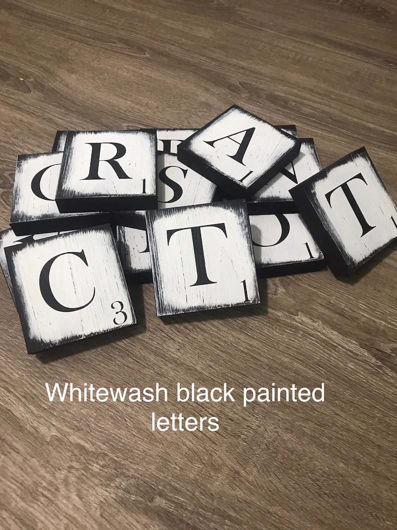 Op de afbeelding: Wit gewassen zwart geschilderde letters. Vierkante houten tegels met zwarte randen en witte, verweerde oppervlakken. Elke tegel heeft een grote zwarte letter. De tekst in de afbeelding luidt: Wit gewassen zwart geschilderde letters.