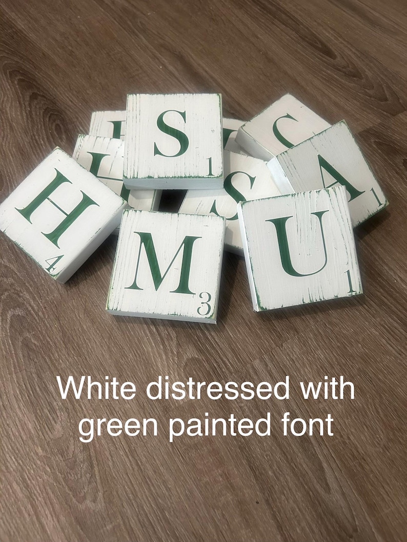 Op de afbeelding: Witte, verweerde houten lettertegels met groen geschilderde letters en cijfers. De letters zijn H, S, M, U en A. De tekst in de afbeelding luidt: "Wit verweerd met groen geschilderd lettertype."
