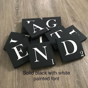 Op de afbeelding: Zwarte vierkante tegels met wit geschilderde letters die "END TAG T" spellen. De tegels zijn in een stapel gerangschikt. De tekst "Solid black with white painted font" staat onderaan de afbeelding.