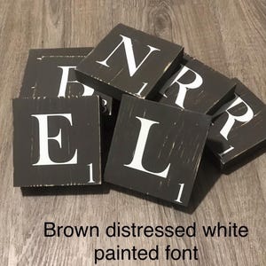 Op de afbeelding: Een verzameling verweerde bruine houten tegels met wit geschilderde letters. De tegels spellen het woord "BELR" en bevatten het nummer "1" op elke tegel. De tekst "Brown distressed white painted font" staat onderaan.