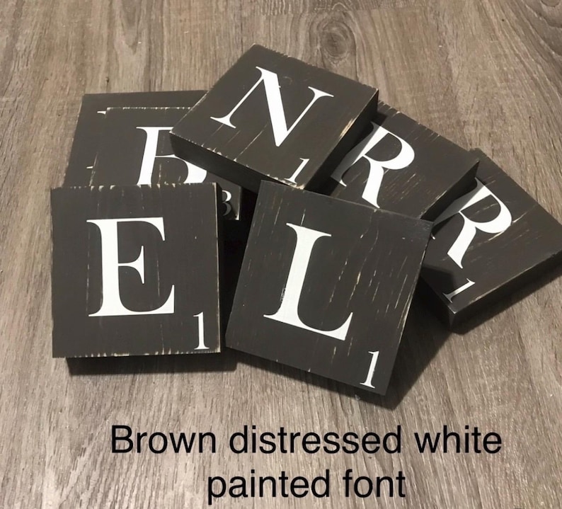 Op de afbeelding: Een verzameling verweerde bruine houten tegels met wit geschilderde letters. De tegels spellen het woord "BELR" en bevatten het nummer "1" op elke tegel. De tekst "Brown distressed white painted font" staat onderaan.