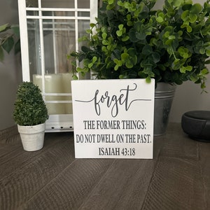Puede incluir: Un letrero de madera blanco con texto negro que dice "olvida las cosas del pasado; no te quedes en el pasado. Isaías 43:18"