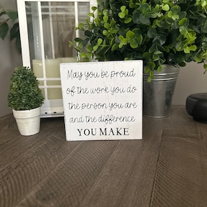 May include: White wooden sign with the text "May you be proud of the work you do the person you are and the difference YOU MAKE".