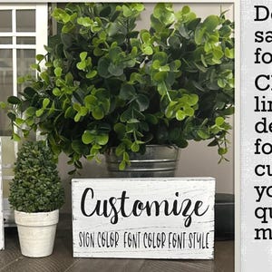 May include: Two rectangular white wooden signs with distressed edges featuring black text that reads Customize, SIGN COLOR, FONT COLOR, FONT STYLE. The signs are displayed alongside a green potted plant and a white lantern frame.