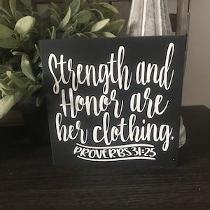 May include: Black wooden sign with white lettering that reads "Strength and Honour are her clothing. Proverbs 31:25"