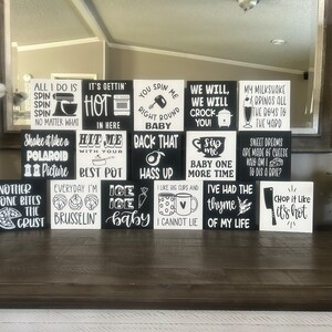 May include: A collection of fifteen square wooden blocks featuring black and white designs with various kitchen-themed puns and song lyrics, including phrases like All I Do Is Spin, Hit Me With Your Best Pot, and Chop It Like It's Hot.
