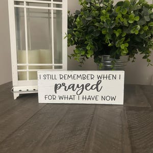May include: White wooden sign with black text that reads "I still remember when I prayed for what I have now".