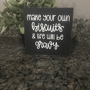 May include: Black wooden sign with white text that reads "Make your own biscuits & life will be gravy".
