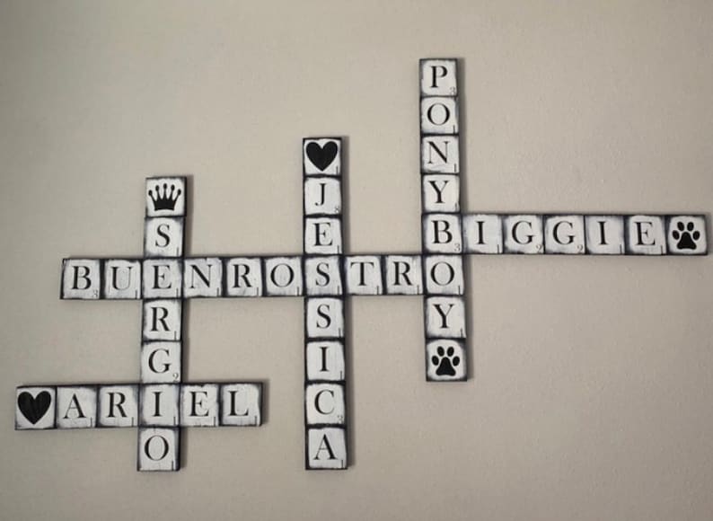 Op de afbeelding: Houten kruiswoordpuzzel muurkunst met zwarte letters op witte blokken. De puzzel bevat namen en woorden als "Ariel", "Biggie" en "Pony". Decoratieve elementen zijn een kroon, harten en pootafdrukken.