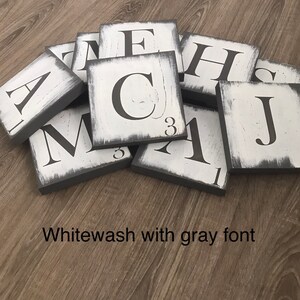 Op de afbeelding: Een verzameling witgekalkte houten lettertegels met grijze randen en grijze letters. De tegels zijn gerangschikt op een houten oppervlak. De tekst "Whitewash with gray font" is zichtbaar.