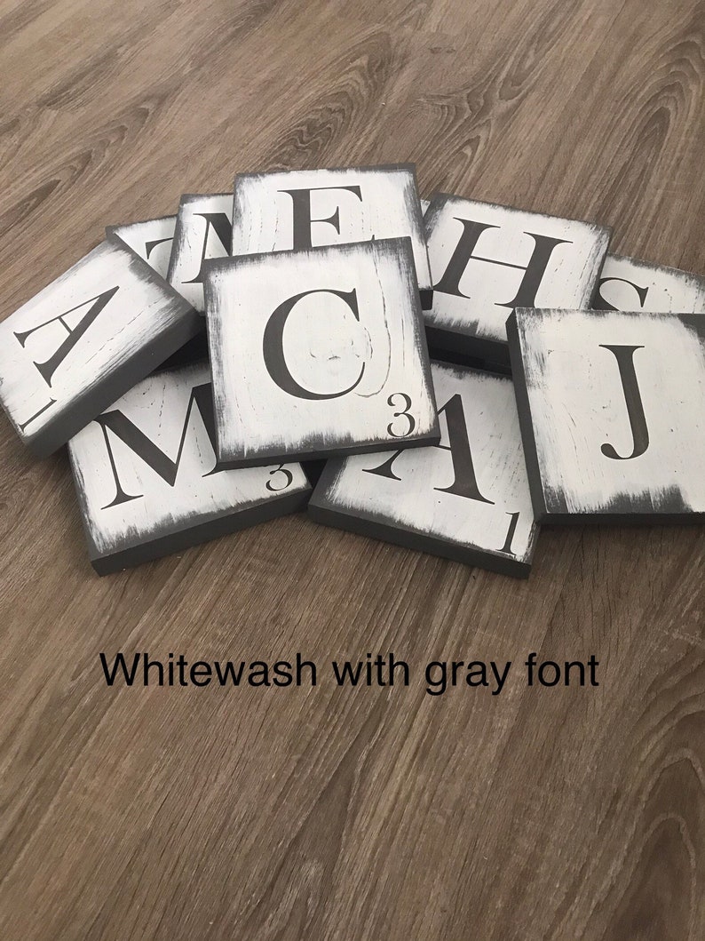 Op de afbeelding: Een verzameling witgekalkte houten lettertegels met grijze randen en grijze letters. De tegels zijn gerangschikt op een houten oppervlak. De tekst "Whitewash with gray font" is zichtbaar.