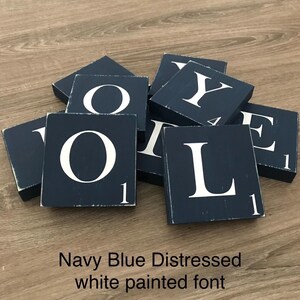 Op de afbeelding: Marineblauwe, verweerde houten blokken met wit geschilderde letters die het woord "LOVE" spellen. Elk blok heeft het nummer "1" in de hoek. De blokken liggen verspreid op een houten oppervlak.