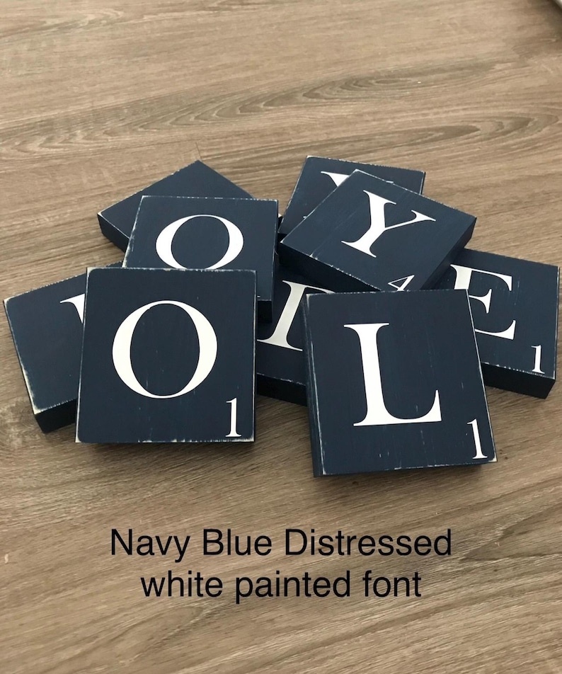 Op de afbeelding: Marineblauwe, verweerde houten blokken met wit geschilderde letters die het woord "LOVE" spellen. Elk blok heeft het nummer "1" in de hoek. De blokken liggen verspreid op een houten oppervlak.