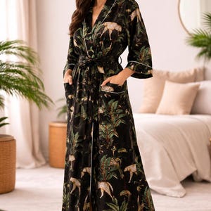 May include: A long black robe featuring a repeating pattern of cheetahs and tropical palm trees in shades of green, tan, and brown. The robe includes a tie waist belt, two front pockets with white piping, and long sleeves with white trim.
