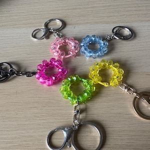 May include: A selection of beaded flower-shaped keyrings in shades of pink, blue, yellow, green, and magenta. Each keyring has a silver-coloured clasp and ring for attaching keys. The faceted beads give a sparkling effect.