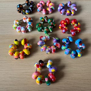 May include: A collection of colorful beaded rings. Each ring features a variety of glass beads in shades of pink, purple, green, yellow, blue, red, and black. The beads are arranged on a silver-colored metal ring.