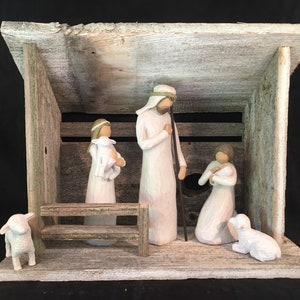 May include: A white wooden nativity scene with a rustic wood frame. The figures are white and include a shepherd, two women, and two lambs. The scene is set in a barn with a wooden bench.