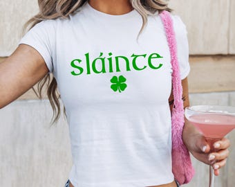 May include: White cropped t-shirt with the Irish phrase "sláinte" in green lettering and a green four-leaf clover.
