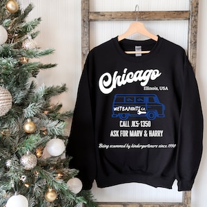 May include: Black sweatshirt with the word "Chicago" in white script. Below, a blue graphic of a van with the text "WET BANDITS CO." and phone number. The text "Being scammed by kindergarteners since 1990" is also visible.