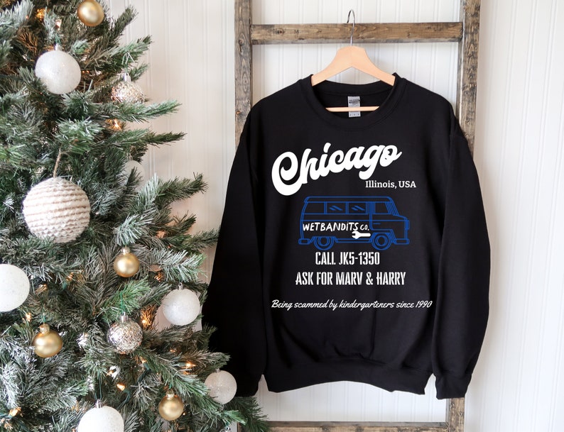 May include: Black sweatshirt with the word "Chicago" in white script. Below, a blue graphic of a van with the text "WET BANDITS CO." and phone number. The text "Being scammed by kindergarteners since 1990" is also visible.