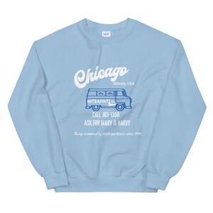 May include: Light blue sweatshirt with white text and a blue graphic. The text reads "Chicago, Illinois, USA" and "WETBANDITS CO." with a van illustration. Additional text includes "CALL JK5-1350" and "ASK FOR MARV & HARRY."