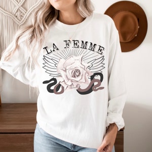 May include: White sweatshirt with a graphic design featuring a rose with wings and a snake, and the text "LA FEMME".
