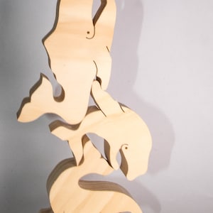 Peut inclure: Une pile de cinq formes de baleines en bois, chacune sculptée dans une pose différente, la queue de la baleine du haut étant rentrée dans la bouche de la baleine du bas. Les baleines sont toutes en bois brun clair.