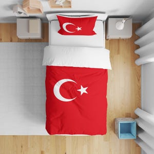 May include: A red and white bedding set featuring the Turkish flag design. The set includes a duvet cover and a pillowcase, both displaying the crescent moon and star emblem. The bed is made up with a white sheet.