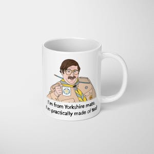 May include: White ceramic mug with a cartoon illustration of a man in a tan jacket and a yellow and blue scarf. The mug has the text "I'm from Yorkshire mate, I'm practically made of tea!" printed on it. The man has glasses and a mustache.