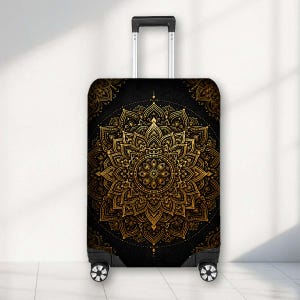 May include: A black suitcase cover featuring a large, intricate gold mandala pattern centred on the front. The design includes symmetrical floral-like petals and geometric details. The cover is fitted onto a rolling suitcase with a silver handle.