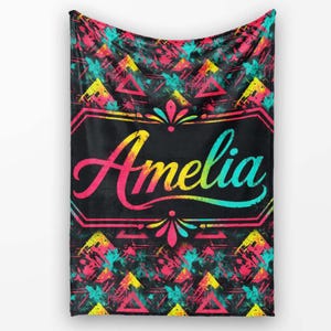 May include: A rectangular throw blanket featuring a black background with a vibrant, multi-coloured splatter pattern of pink, yellow, and teal triangles. The centre displays the name Amelia in a colourful gradient script inside a decorative frame.