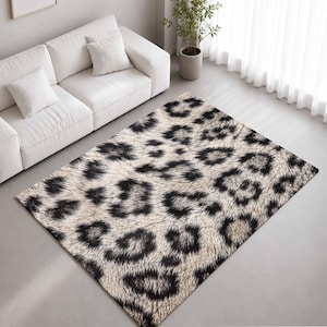 May include: A rectangular area rug featuring a high-contrast leopard print pattern with black spots on a cream and beige background. The rug has a textured, soft-looking surface and is positioned on a smooth, light-coloured floor surface.