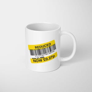May include: White ceramic mug with a yellow "REDUCED" sticker. The sticker includes a barcode and the text "NOW £0.27p". The mug has a curved handle and is set against a white background.