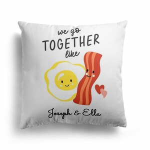 May include: White pillow with the text "We go together like" and a cartoon image of a smiling egg and a smiling piece of bacon. The names "Joseph & Ella" are printed below the image.