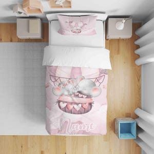 May include: A pink and white baby bedding set with a hot air balloon design and two cartoon elephants. The set includes a duvet cover and pillowcase, with the word "Name" in cursive script.