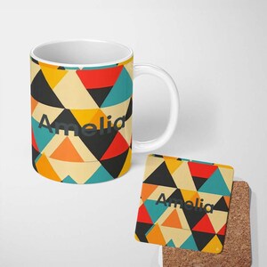 May include: A white ceramic mug and a square cork-backed coaster featuring a geometric pattern of triangles in red, orange, yellow, teal, and black. The name Amelia is printed in dark grey sans-serif letters on both the mug and the coaster.
