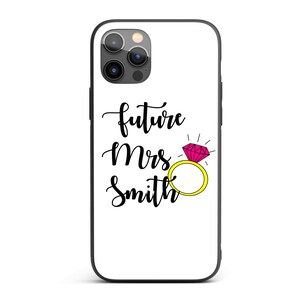 May include: White phone case with a black border. The case displays the text "future Mrs Smith" in a cursive font, along with a pink diamond ring with a gold band. The phone case is designed for a smartphone.