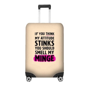 May include: A beige suitcase with a retractable handle and black wheels. The suitcase has the text "IF YOU THINK MY ATTITUDE STINKS YOU SHOULD SMELL MY MINGE" in black and pink.