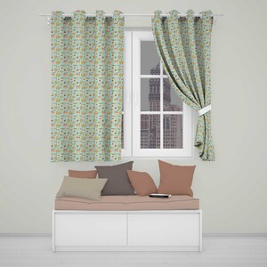 May include: Two light green curtains with a repeating pattern of small colourful cupcakes and sweets hang on a rod. Below, a white bench features a light pink cushion topped with four throw pillows in shades of beige, brown, and muted pink.