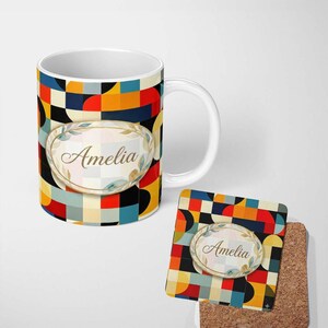 May include: A white ceramic mug and a square cork-backed coaster featuring a colourful geometric pattern of red, orange, blue, black and cream shapes. Both items display a central oval label with a gold border and the name Amelia in script.