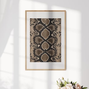 May include: A framed wall art print featuring a repeating snakeskin pattern in shades of brown, tan, and black. The print is centred within a white mat and enclosed in a light-coloured wooden frame, displaying a detailed reptilian scale texture.