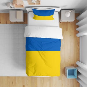 May include: A bed featuring a blue and yellow duvet cover and pillow, with a white top sheet. The bedding is arranged on a white bed frame. The colour scheme is reminiscent of a national flag.