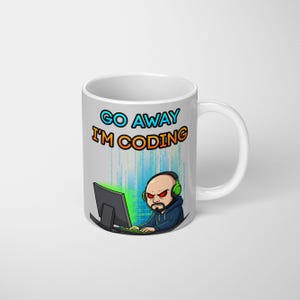 May include: White ceramic mug with a wraparound design featuring a cartoon programmer with headphones and a computer. The text "GO AWAY I'M CODING" is displayed in blue and orange. The programmer has an angry expression.