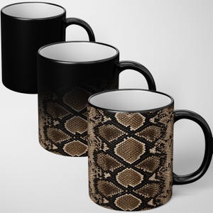 May include: Three ceramic mugs with a white interior and a black handle. The mugs display a heat-sensitive colour-changing effect, transitioning from a solid black exterior to a detailed brown and black snakeskin pattern across the surface.