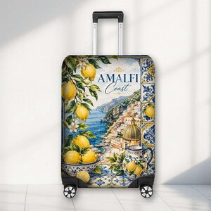 May include: A rolling suitcase featuring a printed design of the Amalfi Coast with yellow lemons, green leaves, blue and white ceramic tiles, and a pitcher. The text AMALFI Coast is printed in blue and gold on the front of the luggage cover.