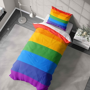 May include: A colourful duvet cover and pillowcase set with rainbow stripes. The bedding displays horizontal bands of red, orange, yellow, green, blue, and purple. The pillowcase is on a white bed, and the duvet cover is partially unfolded.